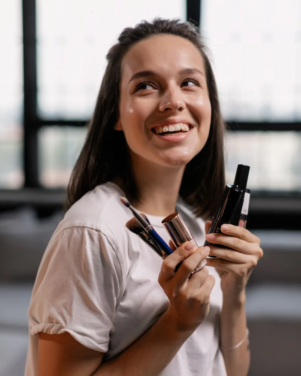 Smiling woman holding makeup brushes, lipstick and cosmetics — beauty and fragrance distributors selling wholesale with their B2B VentasxMayor store