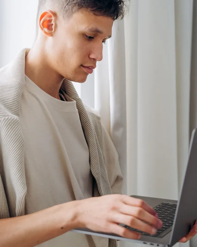 Young man working on a laptop standing by a window — technology and electronics distributors selling wholesale with their B2B VentasxMayor store